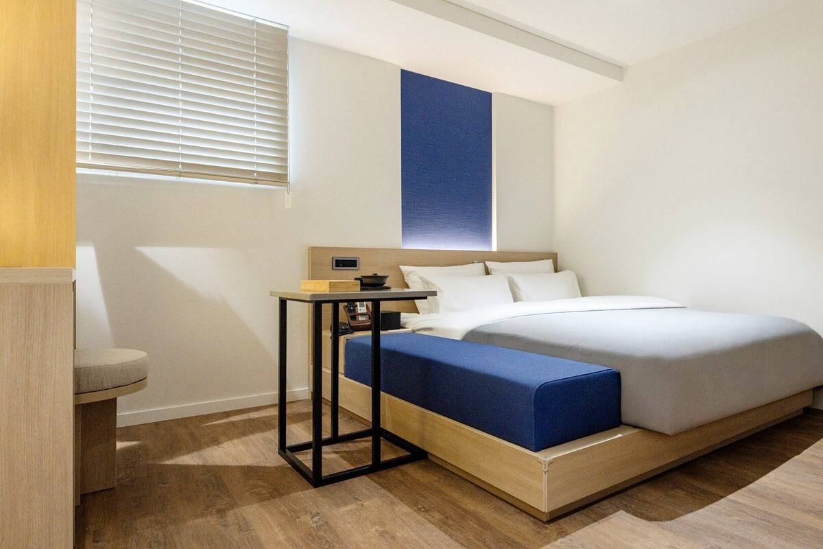 Una habitación de hotel moderna con cama, mesita de noche y una pequeña zona de estar.