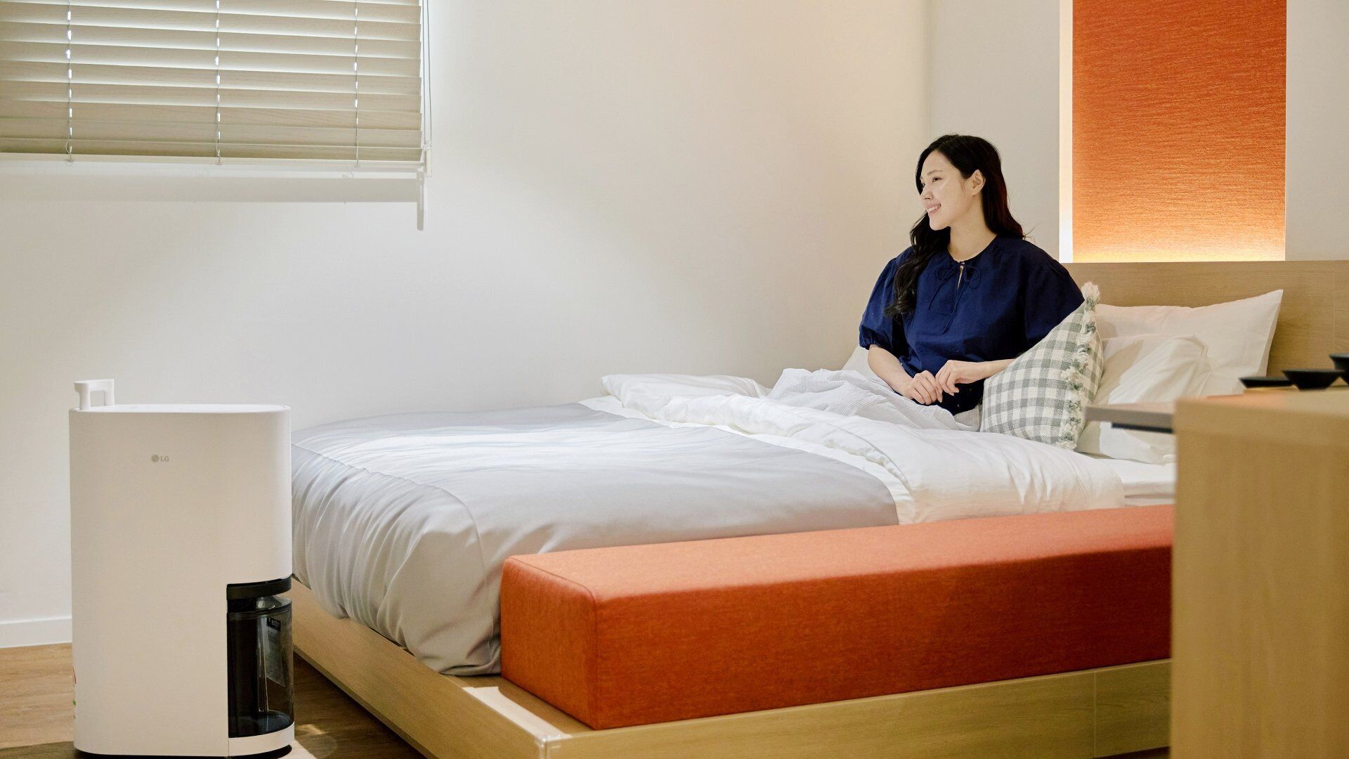 A modern bedroom with a bed, a bedside table, a lamp, and a wall-mounted heater.