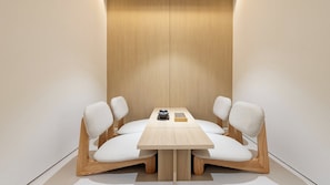 Uma sala de jantar minimalista com uma mesa e cadeiras de madeira, um pequeno objeto preto sobre a mesa e um painel de parede de madeira.