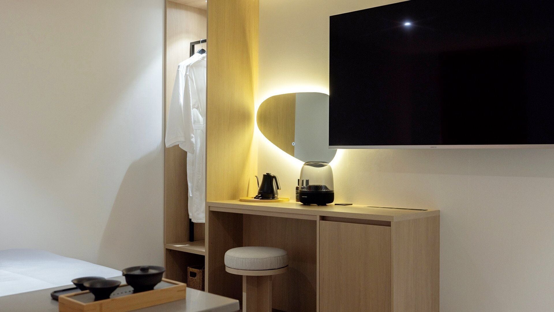 Un baño moderno con tocador de madera, un televisor de pantalla plana montado en la pared, una toalla colgada en un perchero y un taburete pequeño.