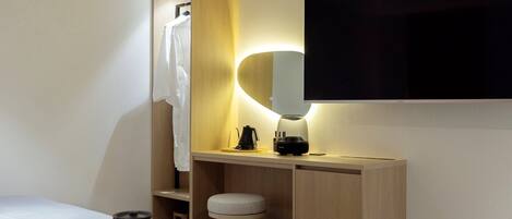 Un baño moderno con tocador de madera, un televisor de pantalla plana montado en la pared, una toalla colgada en un perchero y un taburete pequeño.