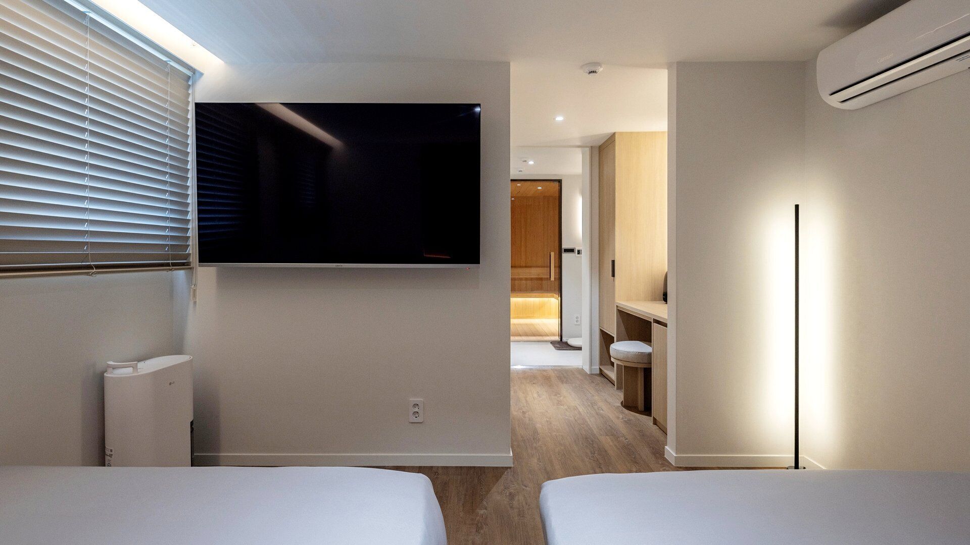 Ein modernes Hotelzimmer mit flachbildfernseher an der Wand, einem Nachttisch, einer Lampe und einem Holzboden.