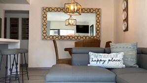 Un salon moderne avec un canapé d’angle gris, un petit coin bar avec des tabourets, un grand miroir doté d’un cadre décoratif et un luminaire suspendu au plafond.