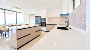 A modern kitchen with a central island, built-in appliances, and a large window providing natural light. - Ocean Skyline Villa-Luxury (Koh Samui)