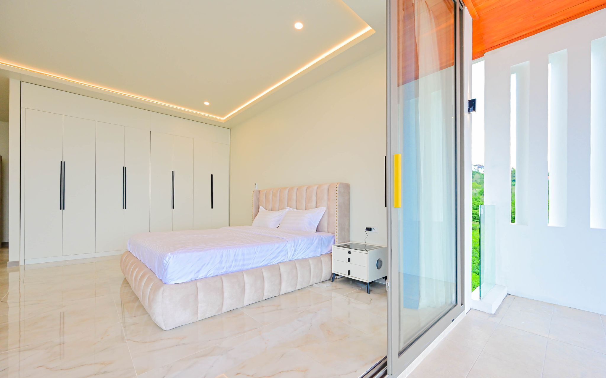 A modern bedroom with a large bed, built-in wardrobe, and a sliding glass door leading to a balcony.