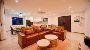A modern living room with a brown leather sofa, two round coffee tables, and a kitchen in the background. - Ocean Skyline Villa-Luxury (Koh Samui)