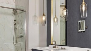 Un bagno moderno con cabina doccia in vetro, un grande specchio con cornice dorata e lampade a sospensione.