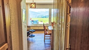 An interior view of a room with a wooden floor, a dining table with chairs, a bench, and a window overlooking a grassy area. - Clair-Azur B 35 by Interhome (Crans-Montana)