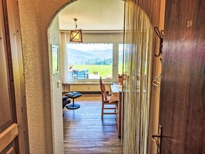 An interior view of a room with a wooden floor, a dining table with chairs, a bench, and a window overlooking a grassy area. - Clair-Azur B 35 by Interhome (Crans-Montana)