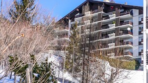A multi-story building with balconies, surrounded by trees and snow. - Clair-Azur B 35 by Interhome (Crans-Montana)