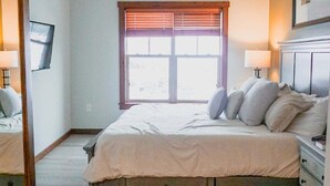 Ein Schlafzimmer mit Bett, Nachttischen, einem Spiegel, einem Fenster mit Jalousien und einer Kommode.