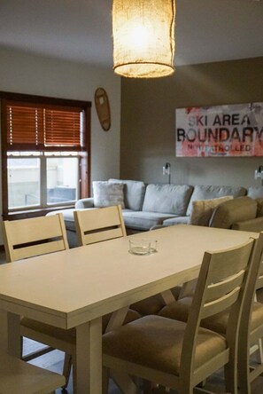Un comedor con una mesa y sillas, una lámpara colgante, un sofá y una ventana con persianas.
