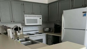 Uma cozinha com ilha central, micro-ondas, fogão, frigorífico e armários cinzentos.