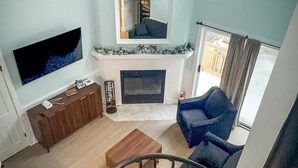 A living room with a TV, fireplace, staircase, and a view of the outside. - Whistlepunk #43: 1 Bedroom With Loft, Slopeside (Snowshoe)