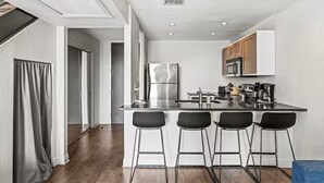 A modern kitchen with a stainless steel refrigerator, a microwave, and a coffee maker. There are four black bar stools at the counter. - Your Amazing Time Ahead - 2BR in Downtown ATX! (Austin)
