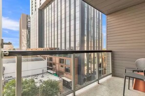 A balcony with a glass railing, a view of a cityscape, and a building with reflective windows. - Your Amazing Time Ahead - 2BR in Downtown ATX! (Austin)