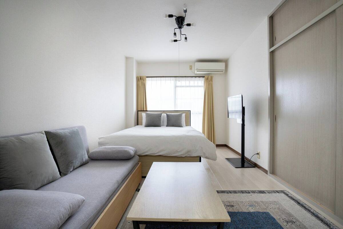 A modern hotel room with a bed, sofa, TV, and a ceiling fan.