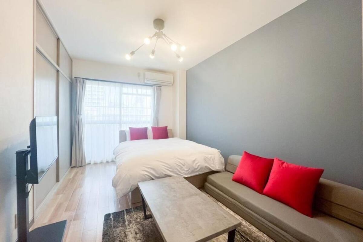A modern hotel room with a bed, a sofa, a TV, and a ceiling light fixture.