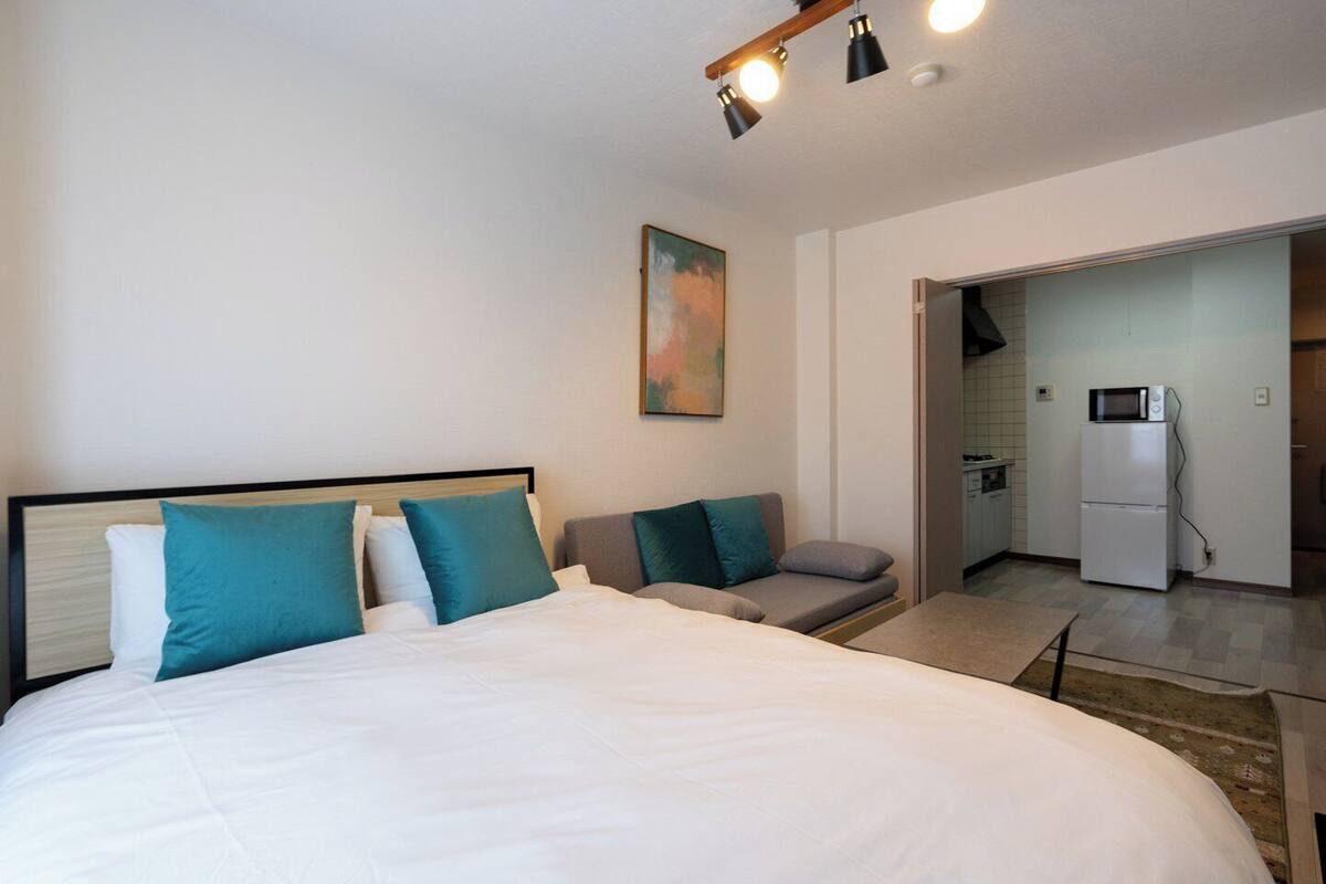 A hotel room with a bed, a sofa, a painting, and a kitchenette.