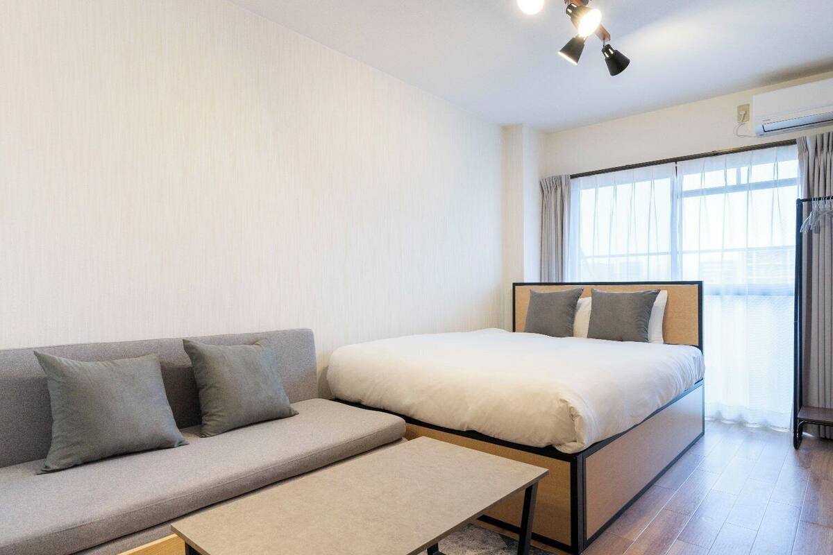 A hotel room with a bed, a sofa, a small table, and a window with curtains.