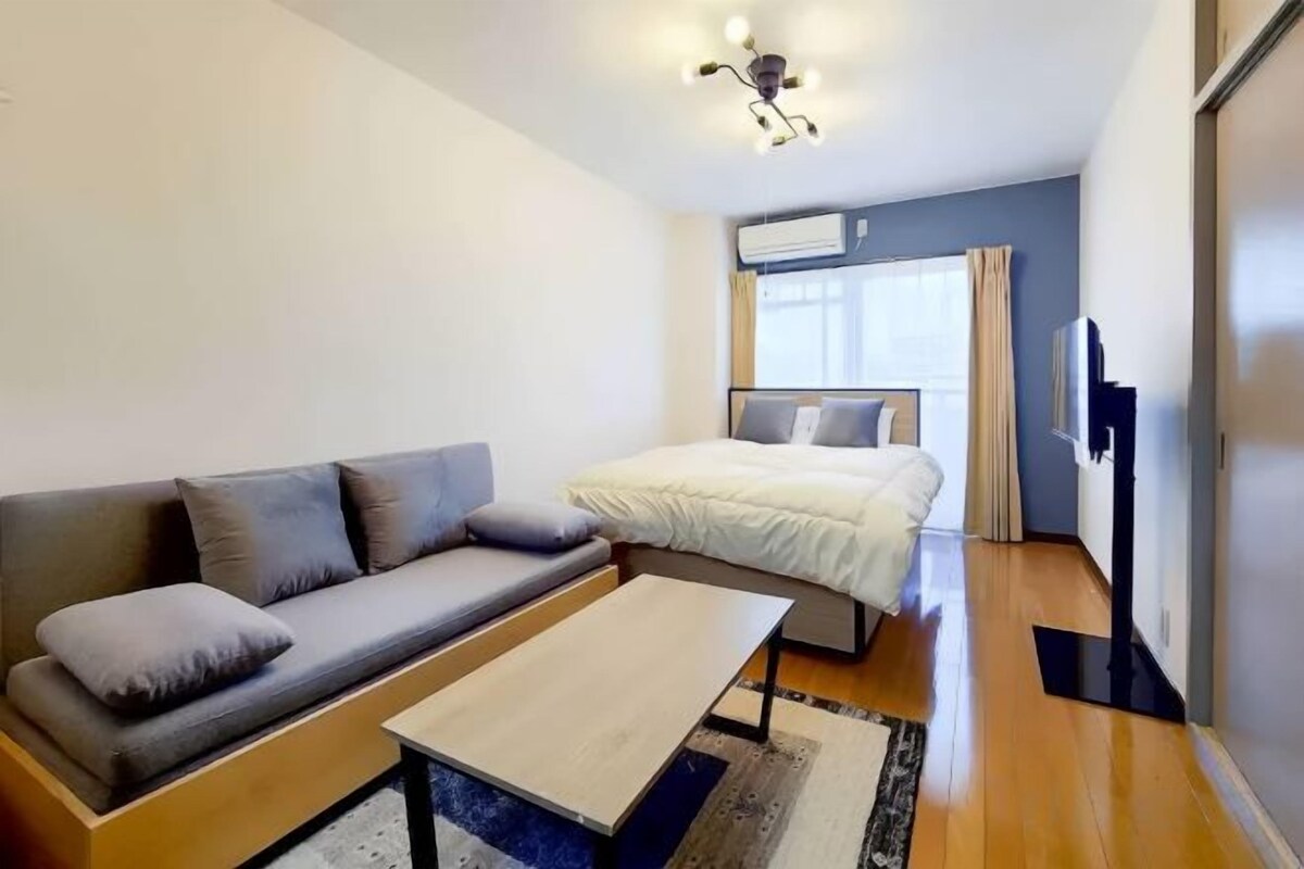 A modern hotel room with a sofa, a bed, a flat-screen TV, and a ceiling light fixture.