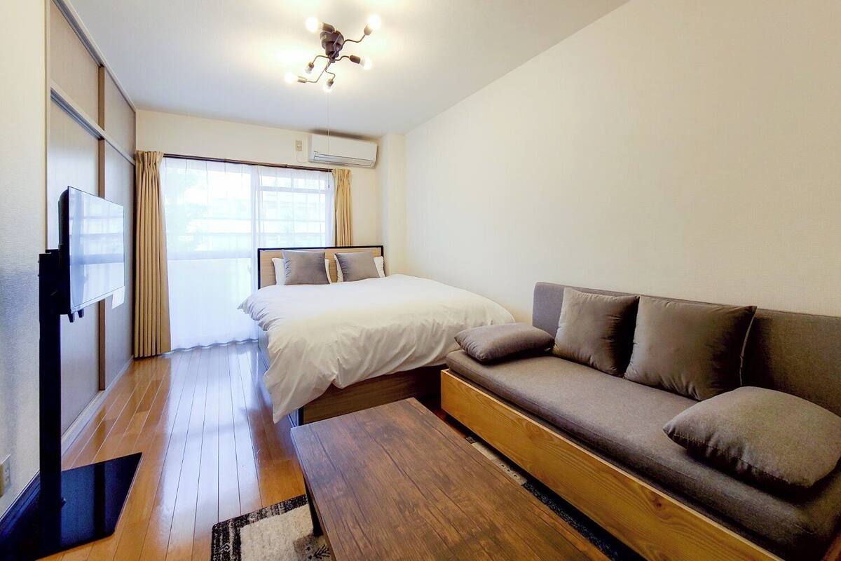 A bedroom with a bed, a sofa, a TV, and an air conditioning unit.