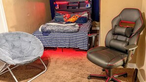 Un dormitorio con una cama, una silla, una mesita y una estantería en la pared.