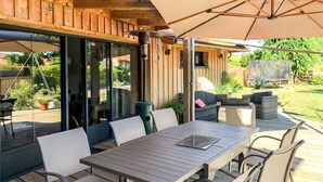 An outdoor patio with a wooden table and chairs, a large umbrella, and a view of the backyard. - Superbe maison avec piscine (Andernos-les-Bains)