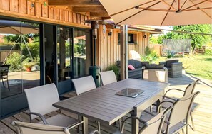 Une terrasse extérieure avec une table et des chaises en bois, un grand parasol et une vue sur le jardin.
