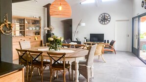 A modern kitchen with wooden cabinets, a dining table with chairs, a hanging orange light fixture, and a clock on the wall. - Superbe maison avec piscine (Andernos-les-Bains)