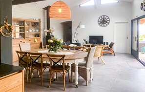 Une cuisine moderne avec des meubles en bois, une table à manger avec des chaises, un luminaire orange suspendu et une horloge au mur.