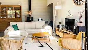 A living room with a sofa, coffee table, wicker chairs, a TV, and a wooden cabinet. - Superbe maison avec piscine (Andernos-les-Bains)