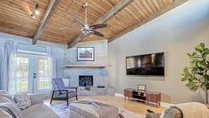 A spacious living room with a fireplace, a ceiling fan, and a large TV. - Luxury 6 Bed Scottsdale Retreat w/ Pool (Scottsdale)