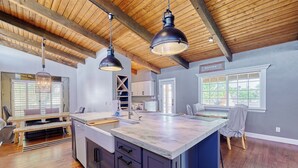 A spacious kitchen with a large island, wooden ceiling beams, pendant lighting, and a view of the outdoors through a window. - Luxury 6 Bed Scottsdale Retreat w/ Pool (Scottsdale)