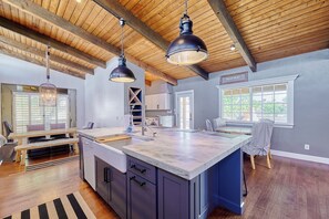 A spacious kitchen with a large island, wooden ceiling beams, pendant lighting, and a view of the outdoors through a window. - Luxury 6 Bed Scottsdale Retreat w/ Pool (Scottsdale)