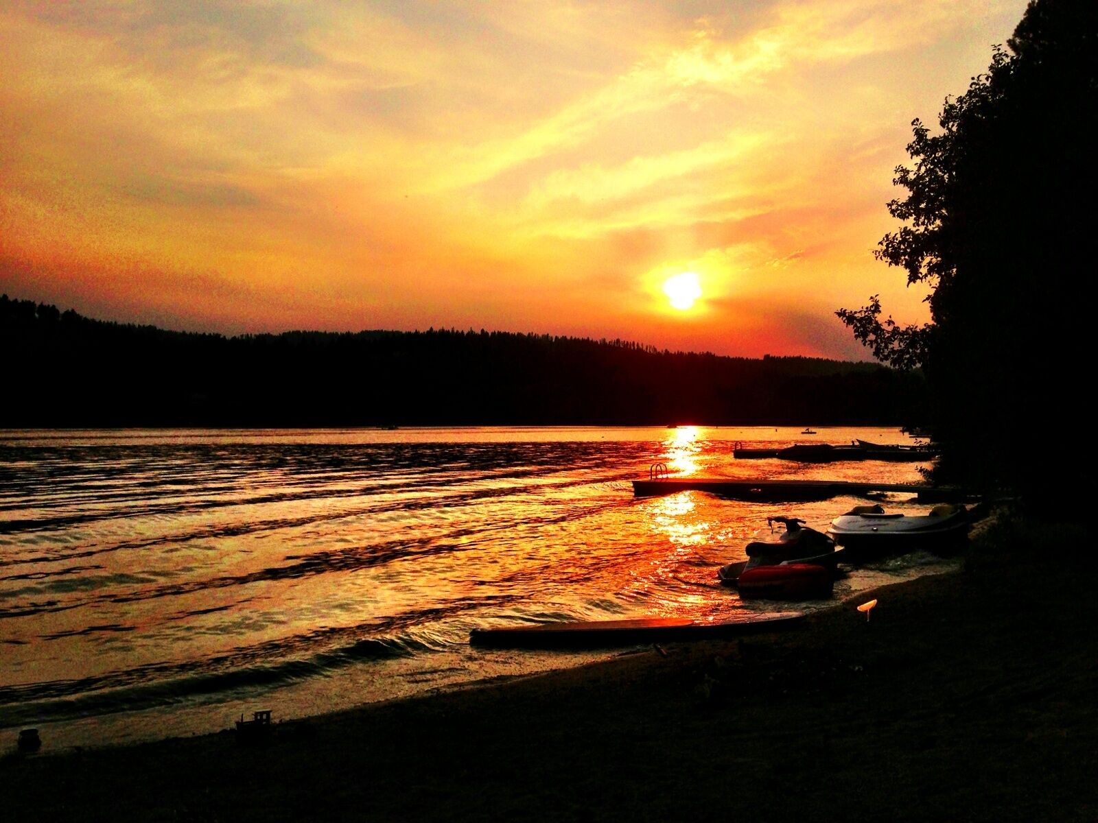 En solnedgång över en stilla sjö med båtar förtöjda längs stranden.
