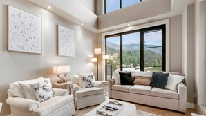 A modern living room with two sofas, a coffee table, and a large window offering a mountain view. - 3 Bed 3 bath Penthouse on Mara, Pool, Gym, Steam room (Sicamous)