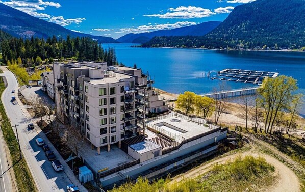 A modern multi-story building with a rooftop terrace, situated near a lake with a dock.