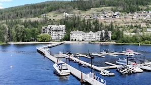 A marina with boats docked, a bridge leading to the shore, and buildings in the background.
