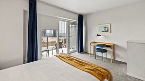 Une chambre d’hôtel avec un lit, un bureau, une chaise, une grande fenêtre et une vue sur la ville.