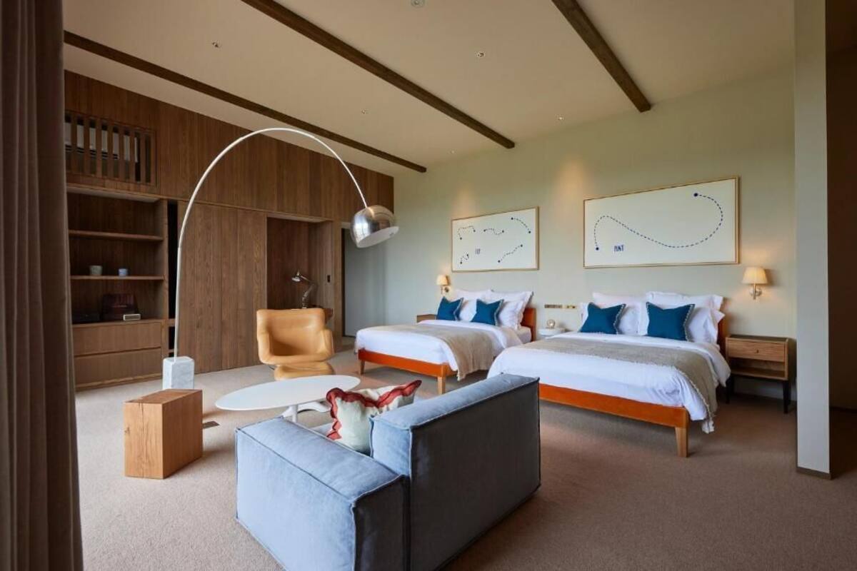A hotel room with two beds, a sofa, a desk, and a bookshelf.