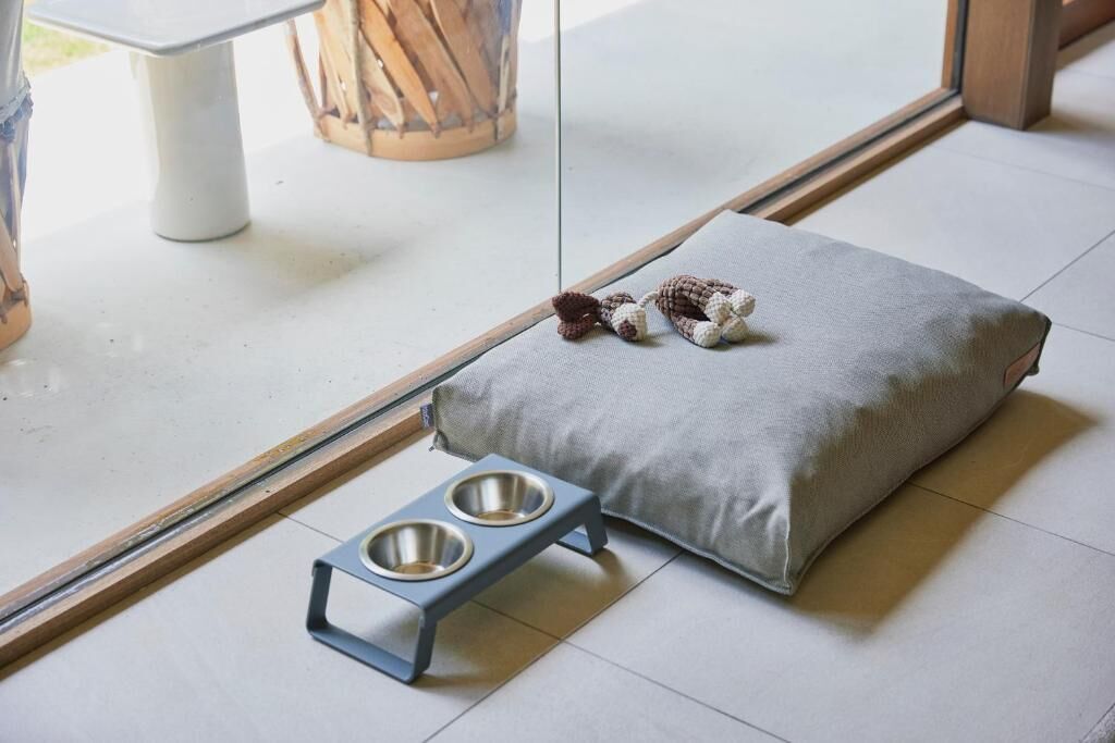 A pet bed with a metal feeding station beside it.