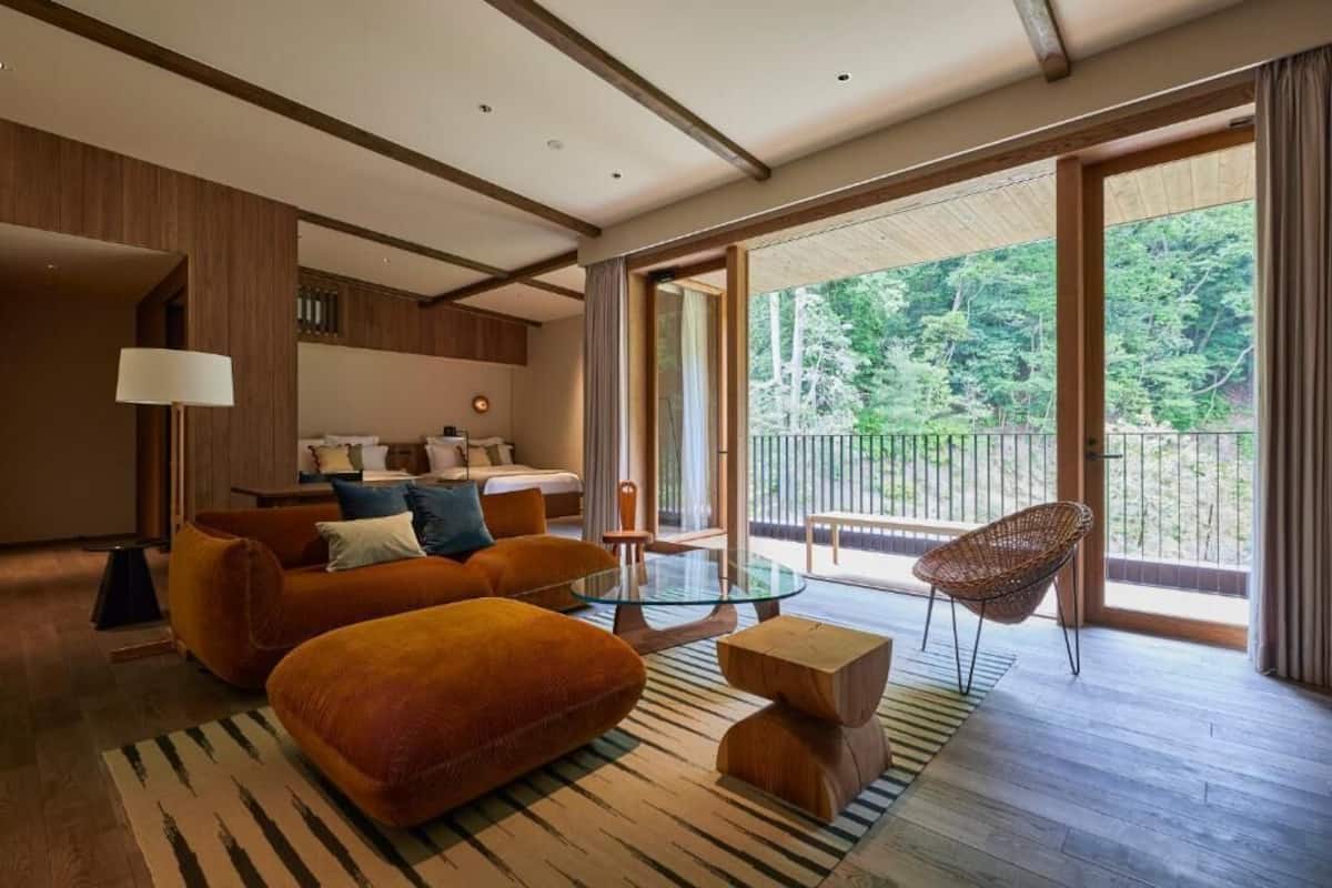 A modern hotel room with a sofa, ottoman, glass coffee table, and a wicker chair.