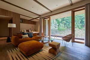 Una habitación de hotel moderna con sofá, reposapiés, mesa de centro de vidrio y una silla de mimbre.