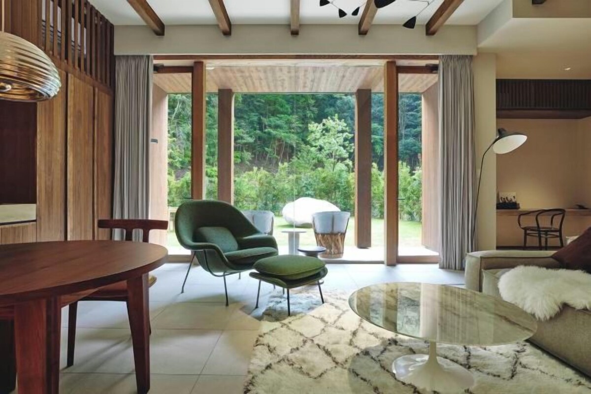 A modern living room with a wooden dining table, green armchair, and a glass coffee table.