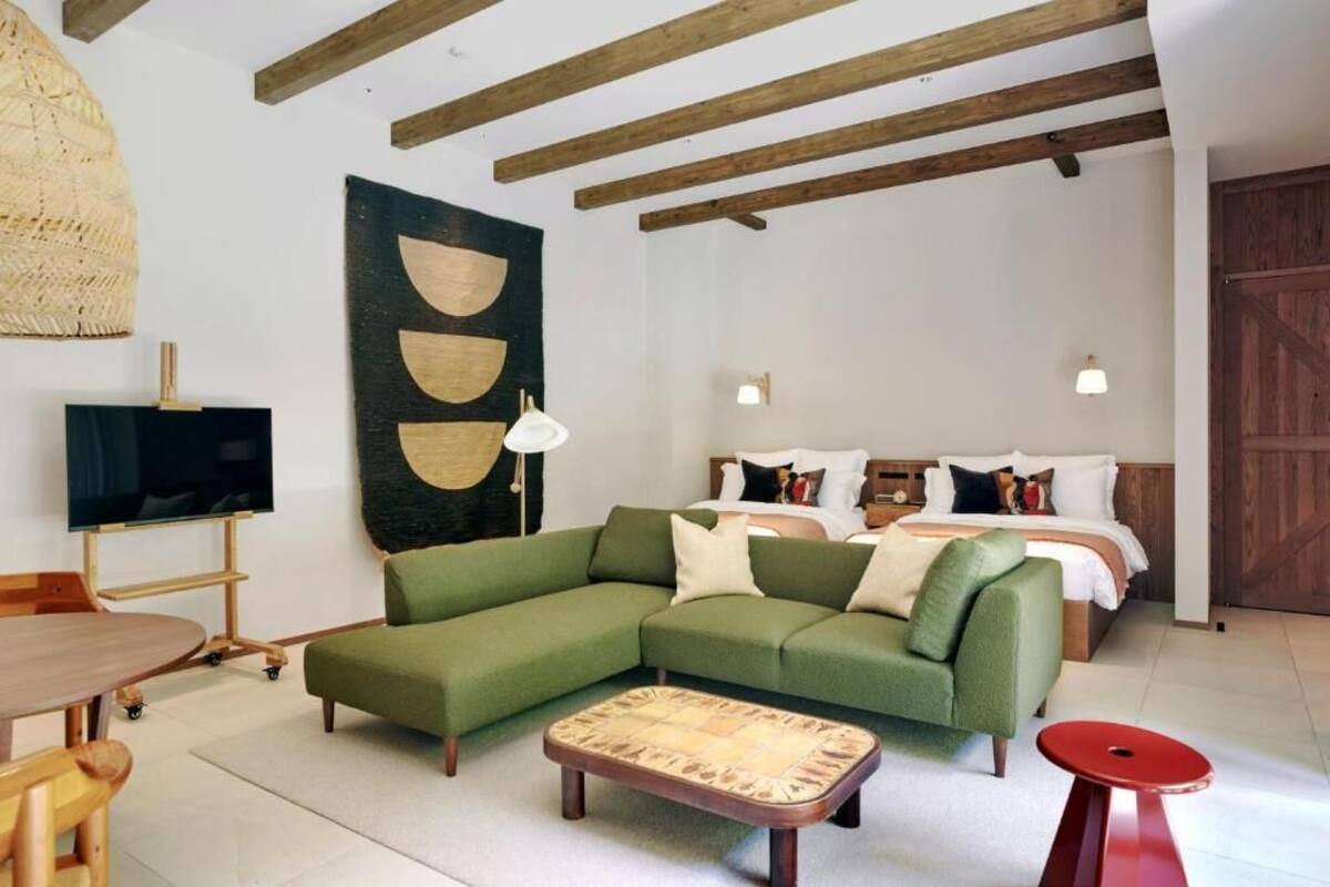 A modern living room with a green sofa, a flat-screen TV, a dining table, and a large wall art piece.