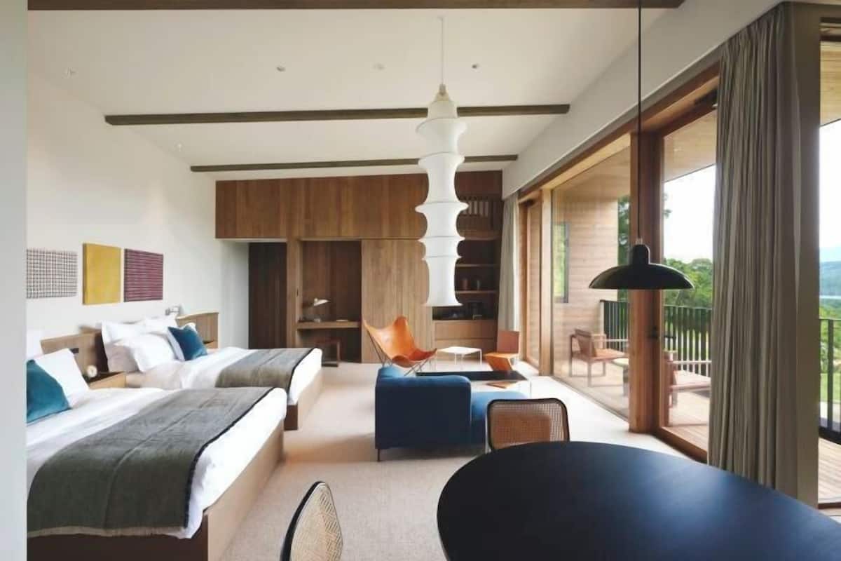 A modern hotel room with two beds, a sofa, a dining area, and a balcony with a view.