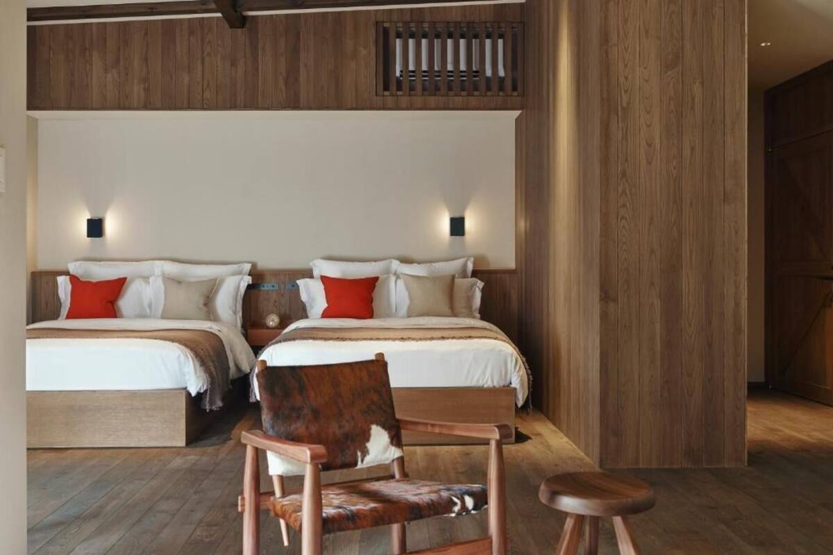 A hotel room with two beds, wooden paneling, and a chair with a leather seat.