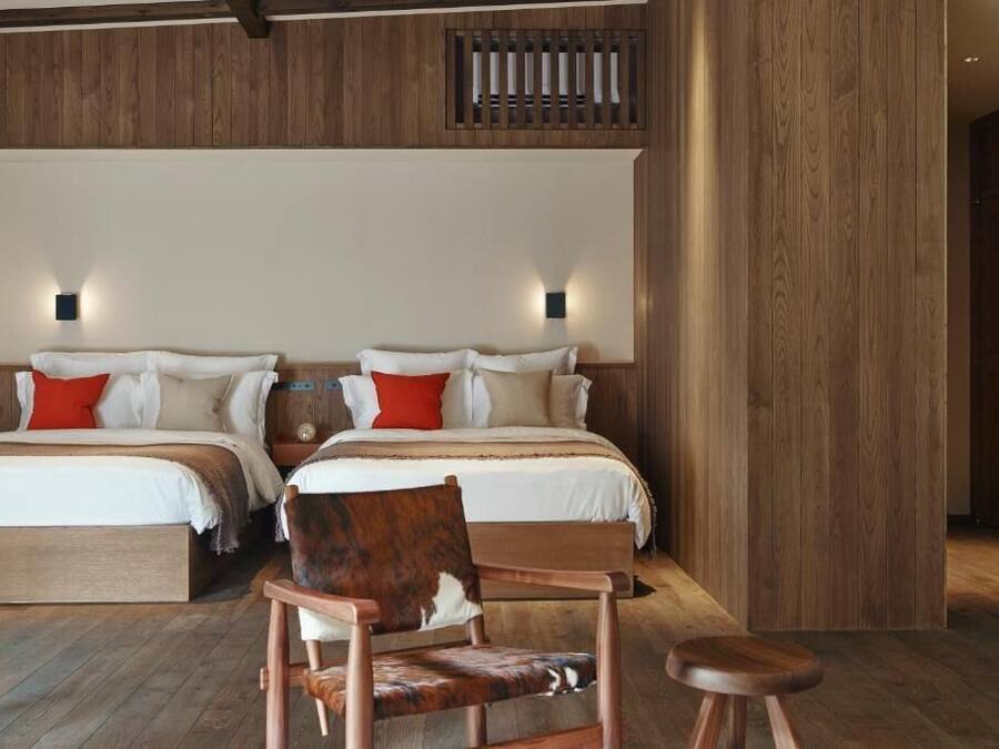 Una habitación de hotel con dos camas, paneles de madera y una silla con asiento de cuero.