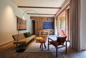Una sala de estar moderna con un sofá, una silla de madera, una mesa de comedor con sillas y una cocina visible a través de una puerta abierta.